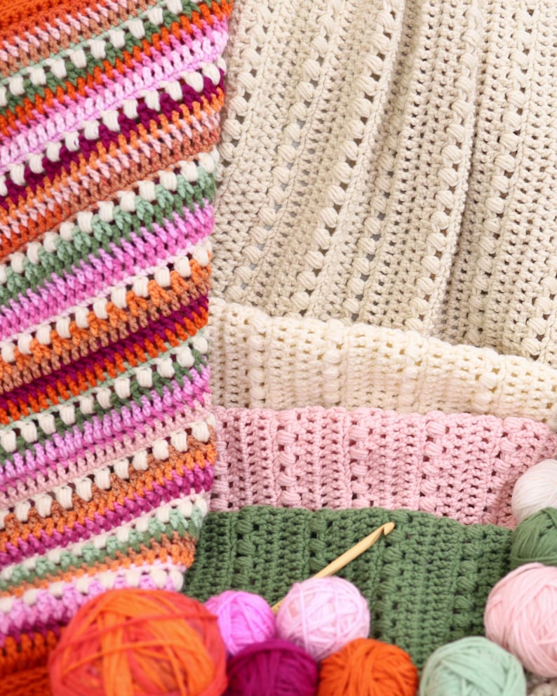 Pu&ograve; includere: Una collezione di articoli all'uncinetto colorati, tra cui coperte e gomitoli di lana. Le coperte presentano vari modelli di punti e combinazioni di colori, come arancione, rosa, verde e crema. Sono visibili anche diversi gomitoli di lana nei toni dell'arancione, del rosa e del verde.
