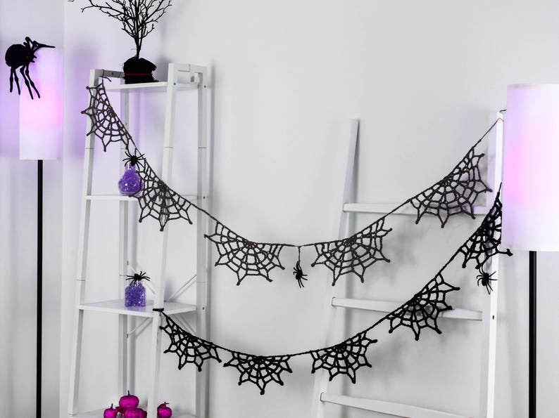 May include: A black crocheted garland featuring multiple spider web motifs connected by a thin string. Small black spider figures are attached to the web segments, creating a decorative hanging piece for seasonal display.