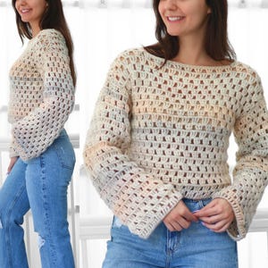 Puede incluir: Un suéter de crochet color crema con mangas largas y acampanadas. El diseño de tejido abierto revela un vistazo a la piel del usuario. El suéter tiene cuello barco y largo recortado, combinado con vaqueros azules.