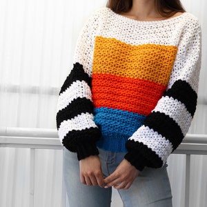 May include: A colorful crocheted sweater with a striped pattern on the sleeves and a horizontal stripe pattern on the body. The sweater is white, yellow, orange, blue, and black.