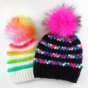May include: Two crocheted hats with colorful stripes and faux fur pom poms. One hat is white with rainbow stripes and the other is black with pink, blue, and white stripes.