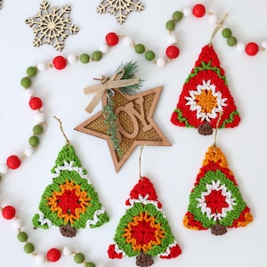 Puede incluir: Cinco adornos de &aacute;rbol de Navidad de ganchillo en rojo, verde, blanco y naranja. Los adornos cuelgan de una cuerda blanca con cuentas rojas y verdes.
