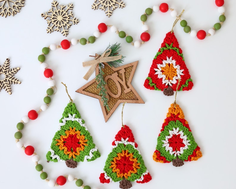 Puede incluir: Cinco adornos de &aacute;rbol de Navidad de ganchillo en rojo, verde, blanco y naranja. Los adornos cuelgan de una cuerda blanca con cuentas rojas y verdes.