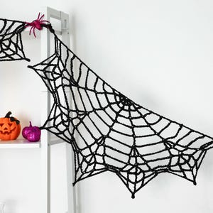 May include: A black crocheted spider web garland featuring intricate web patterns and small, bright pink plastic spiders attached at the connection points, designed for hanging as a decorative Halloween display.