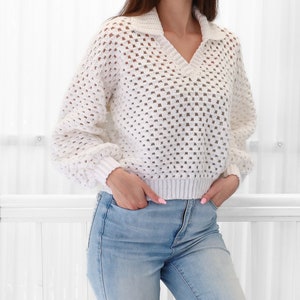 Peut inclure: Pull en crochet blanc avec un col en V et un col montant. Le pull est ample et pr&eacute;sente un design textur&eacute; en tissage ouvert.