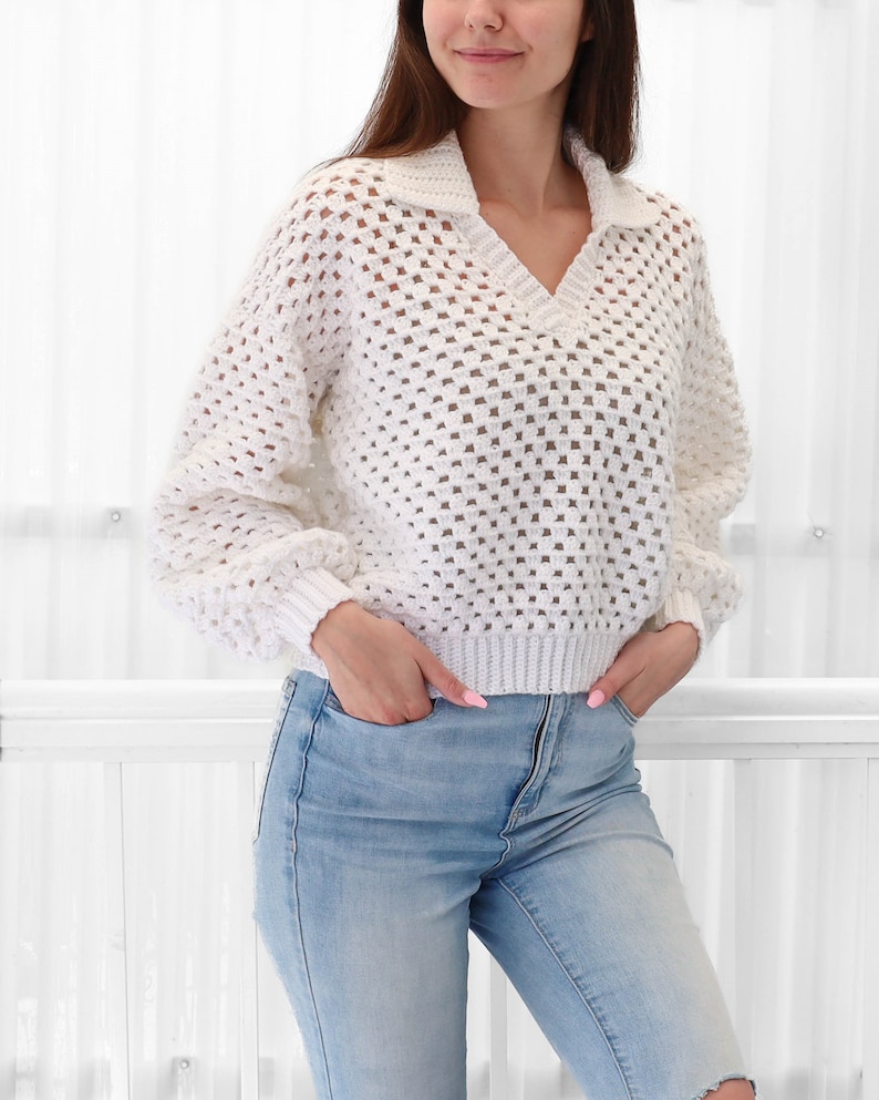 Peut inclure: Pull en crochet blanc avec un col en V et un col montant. Le pull est ample et pr&eacute;sente un design textur&eacute; en tissage ouvert.