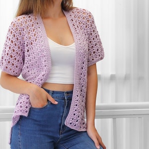 May include: A light purple crochet cardigan with a delicate openwork pattern. The cardigan has short sleeves and a relaxed fit.