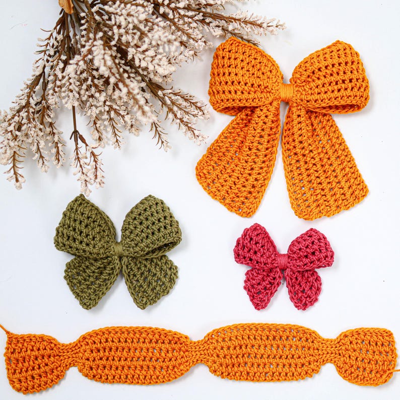 May include: A collection of handmade crochet items including a large orange bow, a medium olive green bow, a small magenta bow, and a long orange rectangular crochet strip, all featuring a textured yarn stitch pattern.