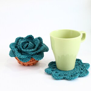 Op de afbeelding: Een turquoise geh&auml;kelde succulent in een terracotta pot naast een lichtgroene mok op een turquoise geh&auml;kelde onderzetter.