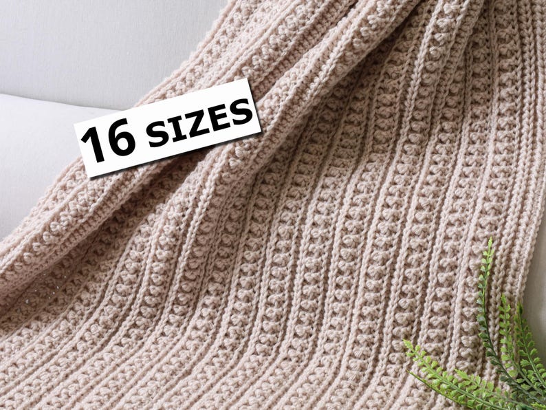 May include: A beige crocheted blanket with a textured pattern. The blanket is folded and displayed on a white surface. The text "16 SIZES" is visible on a white tag.
