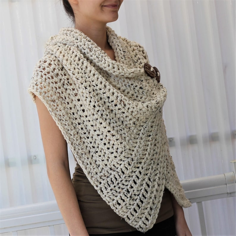 May include: A beige crocheted shawl with a cowl neck and a wooden button closure.
