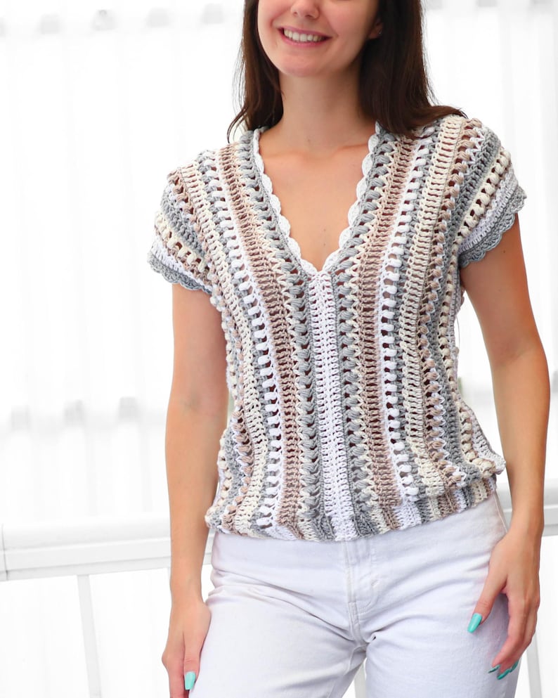 Puede incluir: Top de crochet de manga corta en una paleta de colores neutros de blanco, gris y marr&oacute;n. El top presenta un escote en V con un borde festoneado y una cintura ligeramente fruncida. El patr&oacute;n de crochet crea un dise&ntilde;o texturizado y abierto.