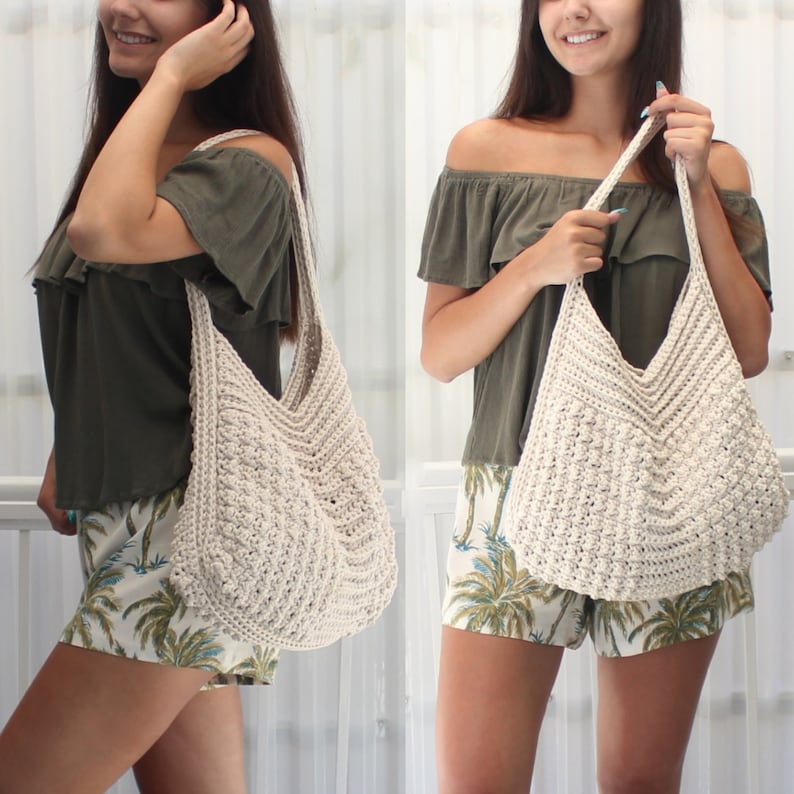 May include: Cream-colored, hand-crocheted tote bag with a wide, open top and long strap. The bag features a textured stitch pattern and a V-shaped design at the top. The bag is shown in a lifestyle shot.