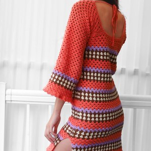 May include: A crocheted dress with a colorful striped pattern in shades of orange, brown, purple, and white. The dress has a scoop neckline and a tie at the back.