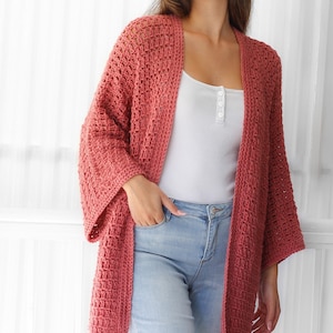 Pu&ograve; includere: Un cardigan all'uncinetto di colore rosa polvere con una vestibilit&agrave; ampia e maniche lunghe. Il cardigan &egrave; aperto sul davanti e ha un design semplice ed elegante.
