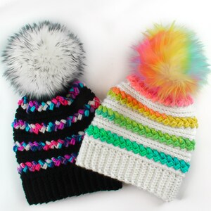 Puede incluir: Dos gorros de ganchillo con pompones de piel sint&eacute;tica. Un gorro es negro con rayas rosas, azules y blancas. El otro gorro es blanco con rayas verdes, amarillas y naranjas.