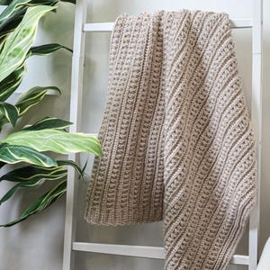 May include: A beige crocheted throw blanket draped over a white ladder.