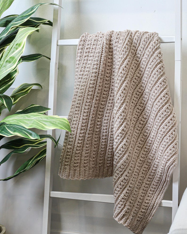 May include: A beige crocheted throw blanket draped over a white ladder.