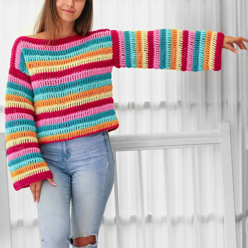Peut inclure: Un pull en crochet ray&eacute; arc-en-ciel &agrave; manches longues. Le pull est court et ample.