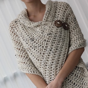 May include: A cream-coloured crocheted poncho with a cowl neck and wooden button fastening.