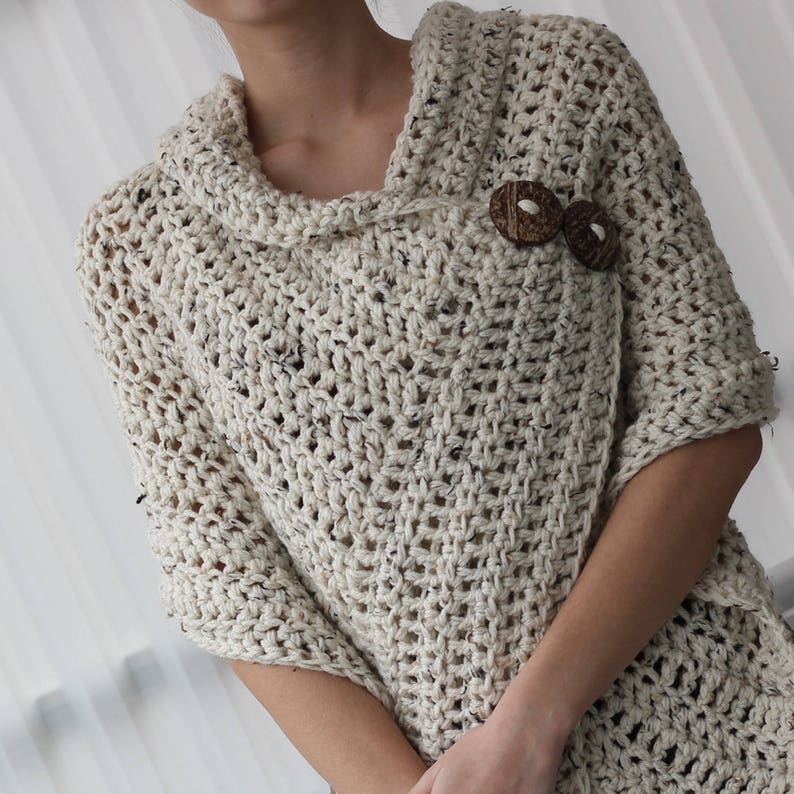 May include: A cream-coloured crocheted poncho with a cowl neck and wooden button fastening.