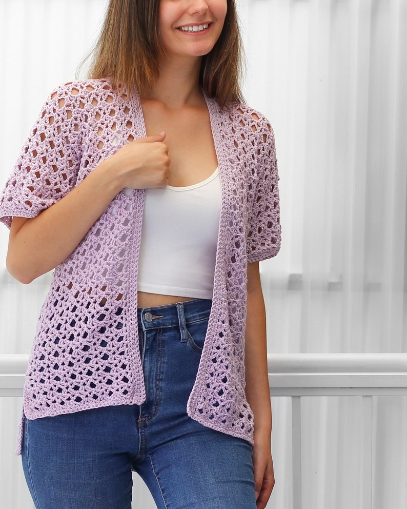 May include: A light purple crochet cardigan with a delicate openwork pattern. The cardigan has a relaxed fit and short sleeves.