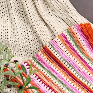 Pu&ograve; includere: Primo piano di due coperte all'uncinetto fatte a mano. Una &egrave; color crema con un motivo strutturato. L'altra &egrave; una coperta colorata con strisce rosa, arancioni, verdi e viola. Le coperte sono piegate e drappeggiate su una superficie.