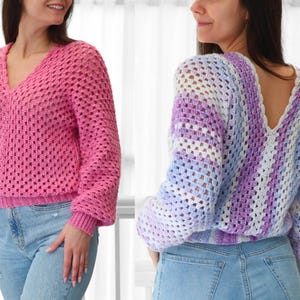 Pode incluir: Dois su&eacute;teres de croch&ecirc;, um rosa e outro com listras azuis, roxas e brancas. Ambos os su&eacute;teres t&ecirc;m um decote em V e s&atilde;o curtos.