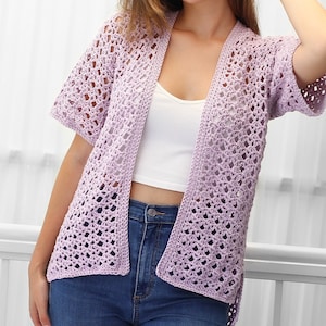 May include: A light purple crochet cardigan with a loose fit and short sleeves. The cardigan is open in the front and has a delicate, lacy pattern.