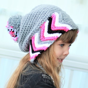 Puede incluir: Un gorro de punto gris con un patrón de chevron rosa, blanco y negro y un pompón esponjoso en la parte superior.