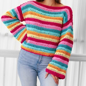 Peut inclure: Un pull en crochet ray&eacute; color&eacute; &agrave; manches longues. Le pull est fait de plusieurs couleurs vives, dont le rose, l'orange, le jaune et le bleu.