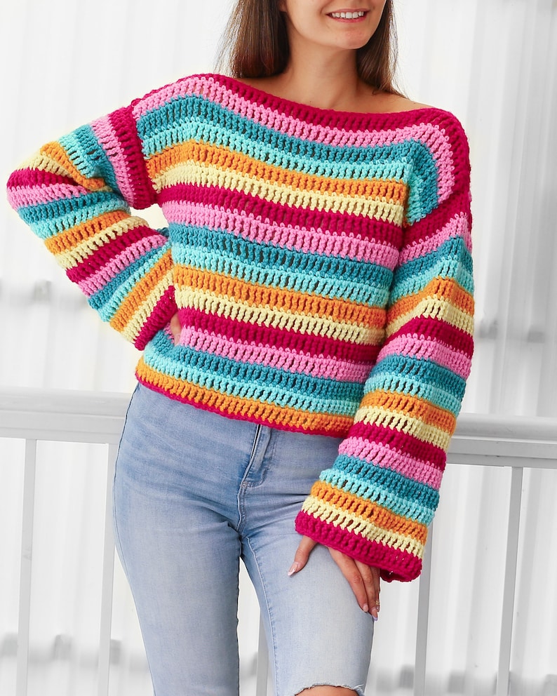 Peut inclure: Un pull en crochet ray&eacute; color&eacute; &agrave; manches longues. Le pull est fait de plusieurs couleurs vives, dont le rose, l'orange, le jaune et le bleu.