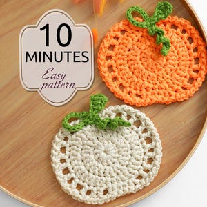 May include: Two round crochet coasters shaped like pumpkins, one orange and one off-white, each with a green stem and curly vine. A beige label with a decorative border displays the text 10 MINUTES Easy pattern in black lettering.