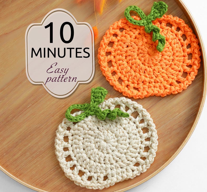 May include: Two round crochet coasters shaped like pumpkins, one orange and one off-white, each with a green stem and curly vine. A beige label with a decorative border displays the text 10 MINUTES Easy pattern in black lettering.