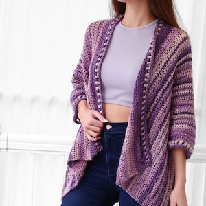 May include: A purple and pink striped crochet cardigan with a slightly open front and a slightly flared hem. The cardigan has a crocheted border with small beads.