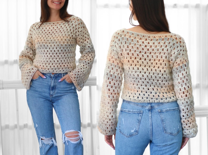 May include: A cream-colored, open-weave crochet sweater with long, flared sleeves. The sweater has a scoop neckline and a subtle color gradient of peach, blue, and gray. The person is wearing light blue ripped jeans.