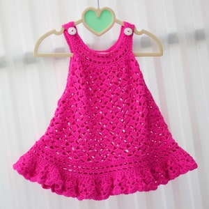 May include: A pink crocheted baby dress with a ruffled hem and white buttons.