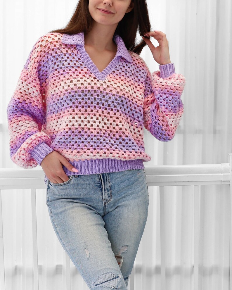Peut inclure: Un pull en crochet ray&eacute; violet clair, rose et blanc avec un col en V et un col montant. Le pull est ample et &agrave; manches longues.