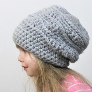 May include: A gray crocheted beanie hat with a slouchy fit. The hat is made with a textured stitch pattern.