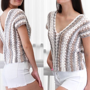 May include: A white crochet top with a v-neck and short sleeves. The top has a striped pattern in shades of white, brown, and gray.