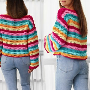 Peut inclure: Un pull en crochet ray&eacute; arc-en-ciel &agrave; manches longues. Le pull est de style court et est fait de plusieurs couleurs, dont le rose, le jaune, l'orange, le bleu et le vert.