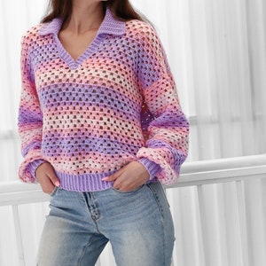 Peut inclure: Un pull en crochet ray&eacute; dans les tons de violet, rose et blanc. Le pull a un col en V et un col.
