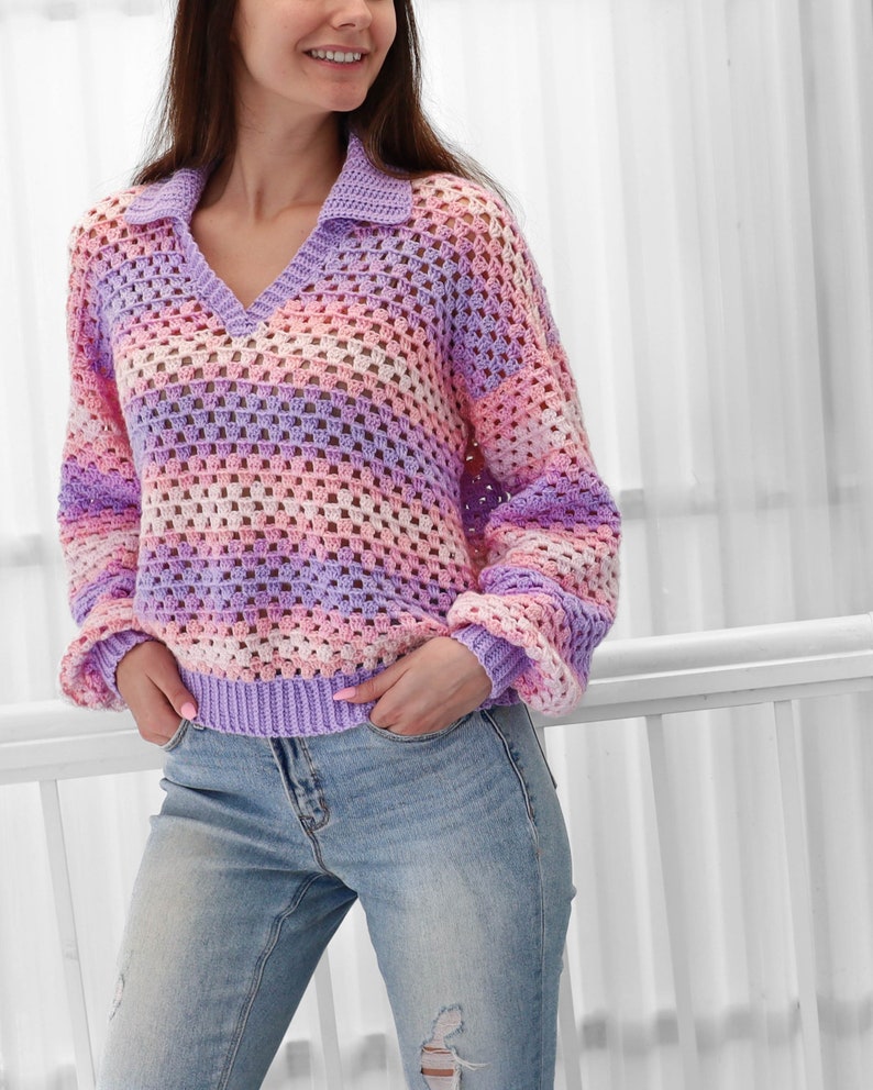 Peut inclure: Un pull en crochet ray&eacute; dans les tons de violet, rose et blanc. Le pull a un col en V et un col.