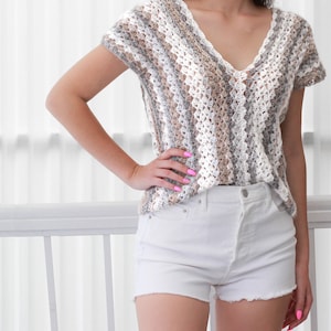 May include: A crocheted top with a V-neck and short sleeves. The top is made with a striped pattern in shades of white, gray, and brown.