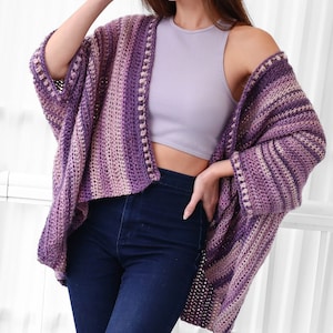 May include: A purple and pink striped crochet cardigan with a crocheted border. The cardigan is open in the front and has long sleeves.