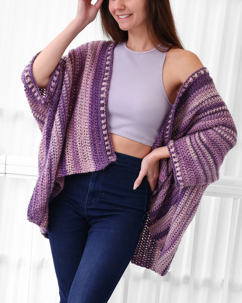 May include: A purple and pink striped crochet cardigan with a crocheted border. The cardigan is open in the front and has long sleeves.
