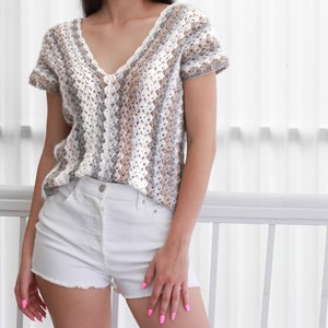 May include: A crocheted top with a striped pattern in shades of white, gray, and brown. The top has a V-neck and short sleeves.