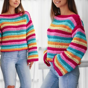 Peut inclure: Un pull en crochet ray&eacute; color&eacute; &agrave; manches longues et &agrave; la coupe ample. Le pull est r&eacute;alis&eacute; avec une vari&eacute;t&eacute; de couleurs vives, dont le rose, le bleu, le jaune et l'orange.