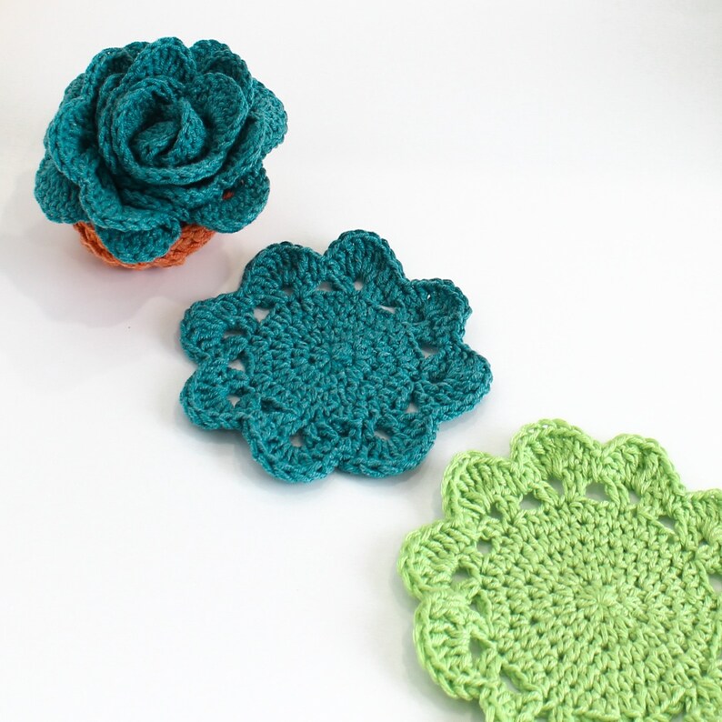 Op de afbeelding: Drie gehaakte onderzetters in de vorm van bloemen. De onderzetters zijn turquoise, groen en lichtgroen.