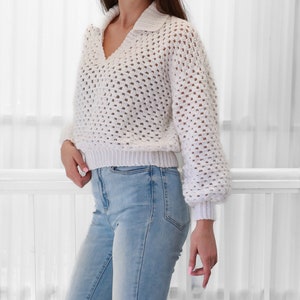 Peut inclure: Pull en crochet blanc &agrave; col et manches longues. Le pull est ample et pr&eacute;sente un motif textur&eacute;. Le mannequin porte le pull avec un jean bleu.
